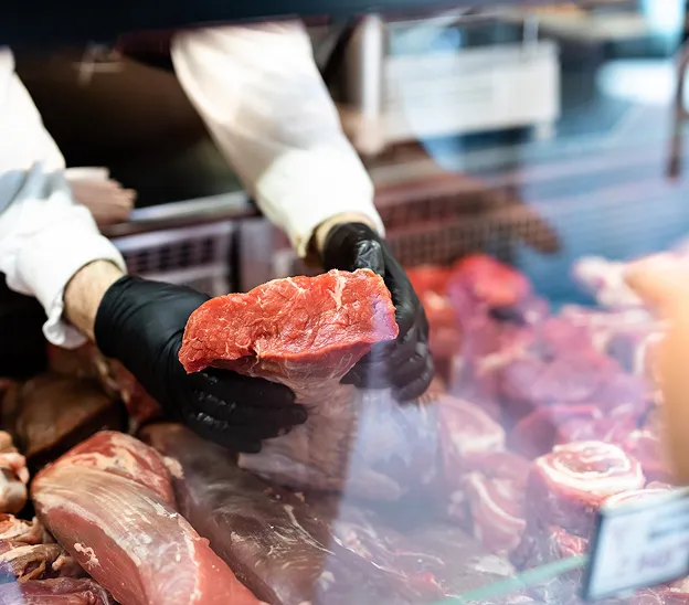 Boucher ganté tenant un morceau de viande rouge au-dessus d'un étalage à Palaiseau en Essonne 91